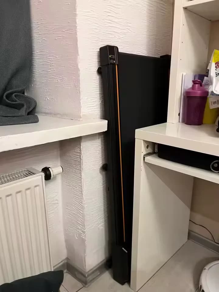 De loopband rechtop opgeborgen naast een kast
